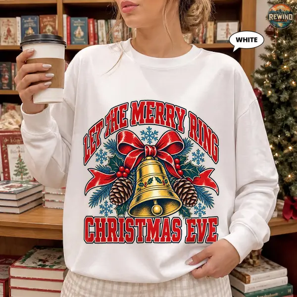 White crewneck sweatshirt with a retro badge print of a Christmas bell, holly and pinecones and Let the Merry Ring wording for a cozy holiday look.