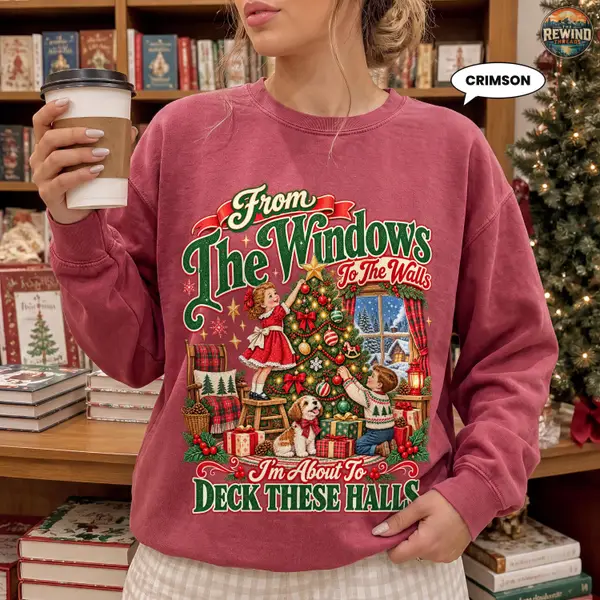 Crimson red Christmas crewneck worn by a woman holding a coffee cup, featuring a nostalgic tree-trimming kids design and Deck These Halls text.