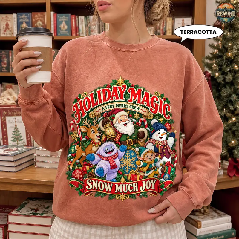 Woman wearing a terracotta crewneck sweatshirt with a retro Holiday Magic Christmas print of Santa, reindeer, snowman, furry snow creature and elf under a Snow Much Joy banner, holding a coffee cup.