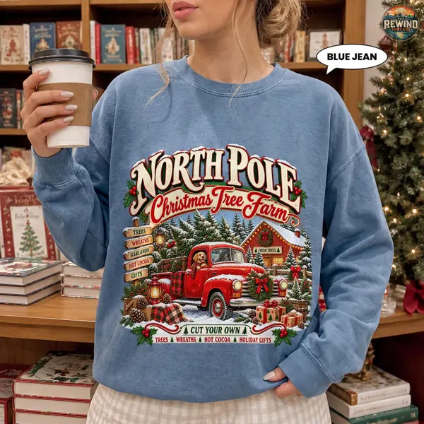 Model wearing a Blue Jean Christmas sweatshirt with a vintage North Pole Christmas Tree Farm design featuring a red pickup truck and snowy holiday scenery.