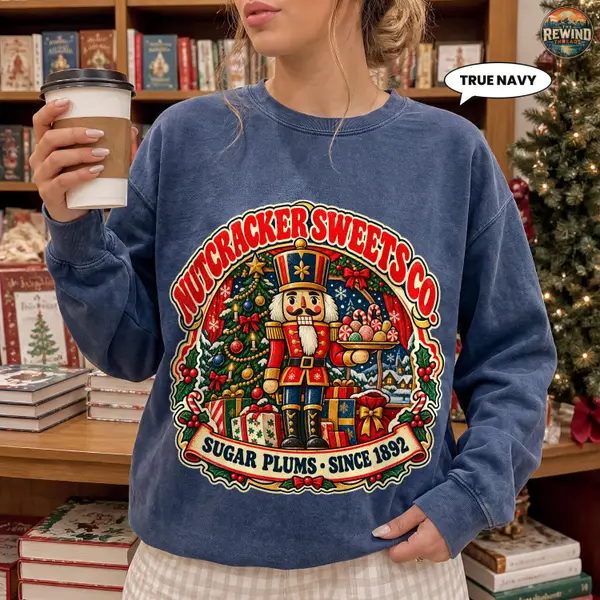 Model wearing a navy blue crewneck sweatshirt with a vintage Nutcracker Sweets Co. print featuring a Christmas toy soldier, candy, a tree and presents.