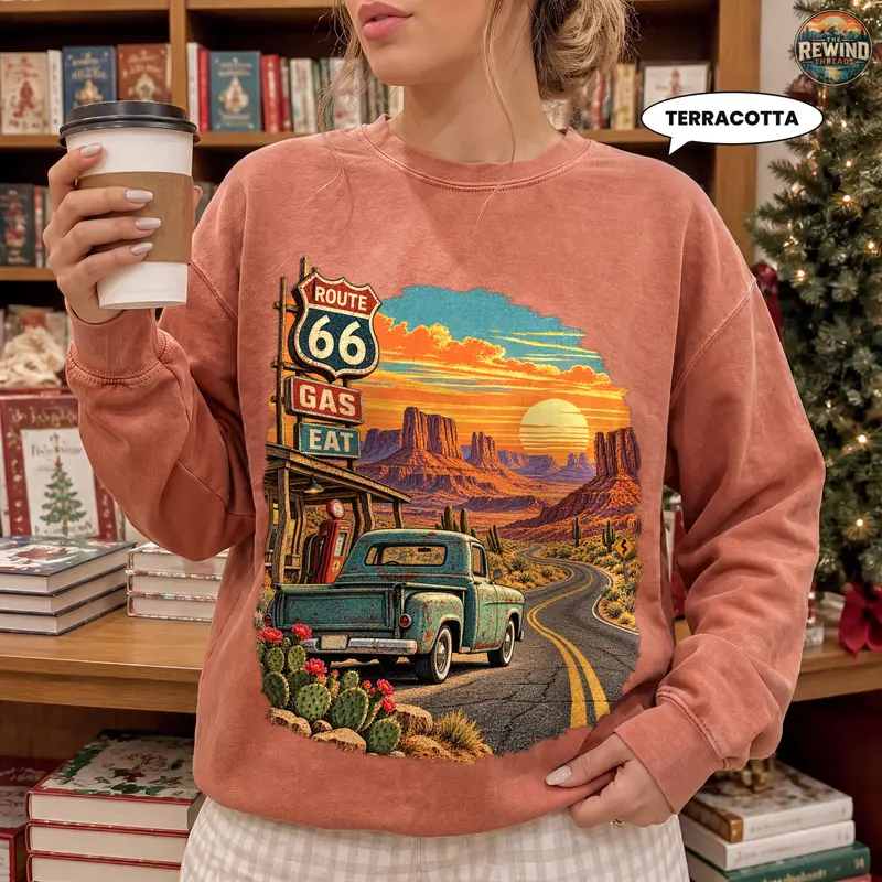 Woman in a terracotta clay crewneck sweatshirt showing a retro Route 66 highway print with desert sunset, vintage pickup truck and cactus flowers.